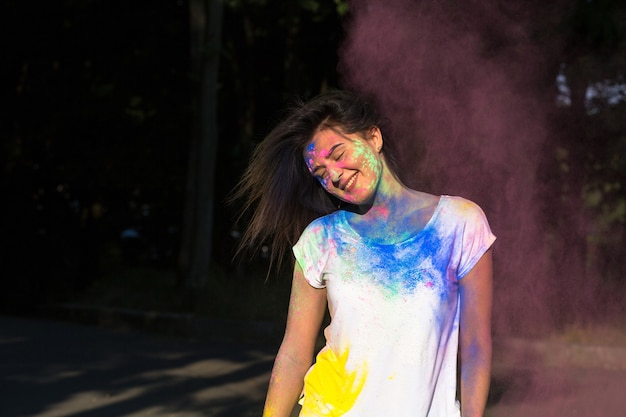 Menina morena positiva posando com pó de Gulal explodindo no parque