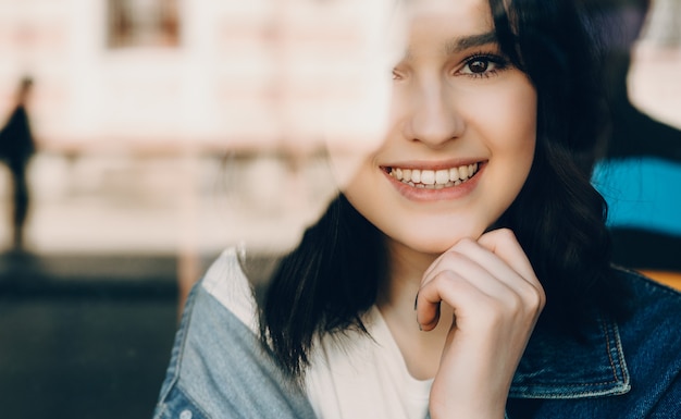 Foto menina morena sentada na frente da janela olhando para a câmera