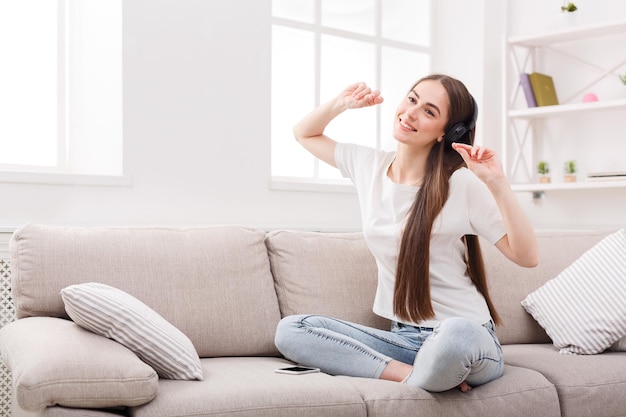 Menina morena sorridente estalando os dedos e ouvindo música online no smartphone em fones de ouvido. Conceito de tecnologia e prazer.