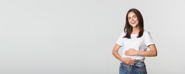 Menina morena sorridente satisfeita esfregando a barriga depois de comer uma comida deliciosa