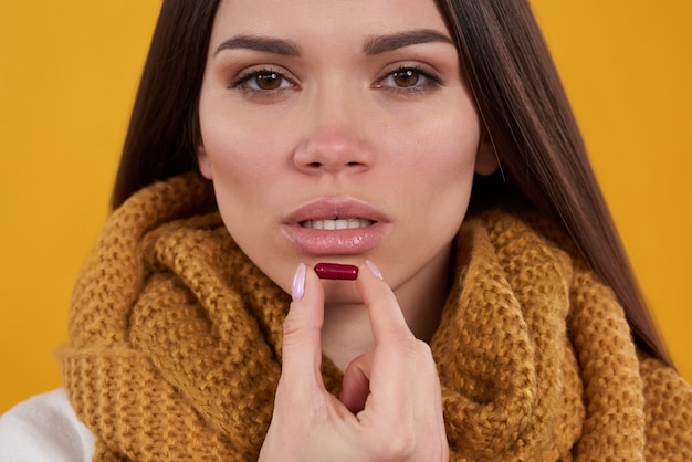 Menina morena tem poses frias com comprimidos em fundo amarelo