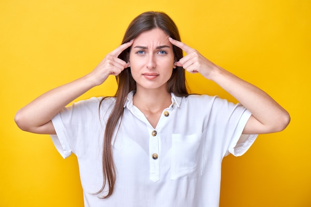 Menina morena tensa segurando os dedos nas têmporas, pensa muito e faz uma escolha isolada em um fundo amarelo