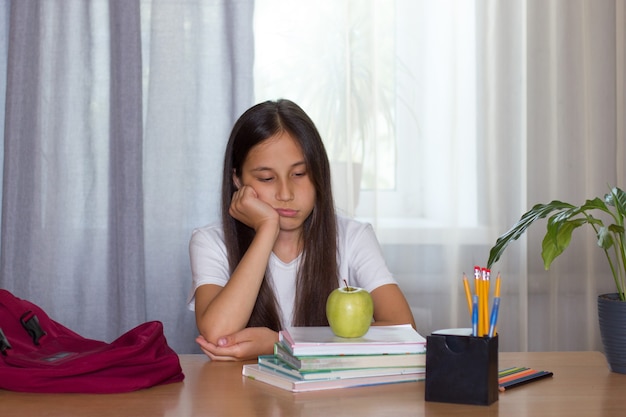 Menina morena triste sentada em casa lendo livros em que há uma maçã no conceito de volta às aulas