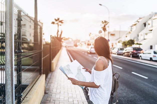 Menina moreno bonita do turista com o mapa nas mãos na rua que procura a maneira.