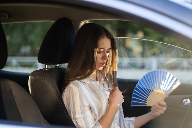 Menina motorista com ventilador de mão sofrendo de calor no carro e tem problema com o ar-condicionado que não funciona