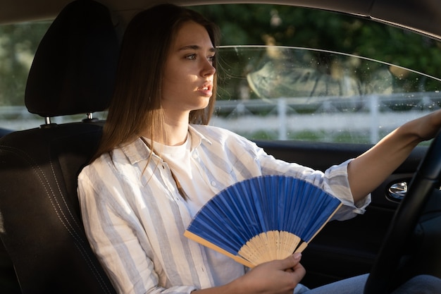 Menina motorista com ventilador de mão sofrendo de calor no carro e tem problema com o ar-condicionado que não funciona