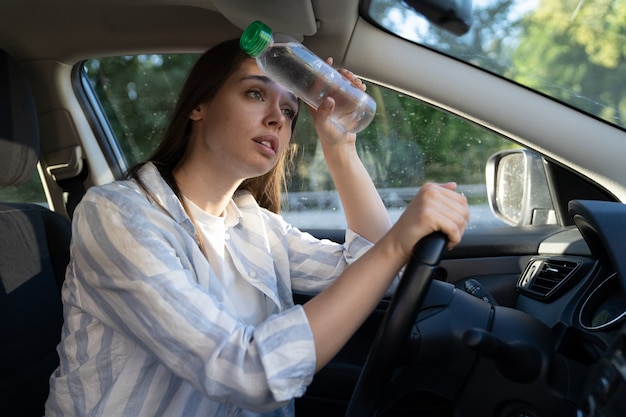 Foto menina motorista exausta, sofrendo de dor de cabeça, calor, clima quente e aplica garrafa de água na testa