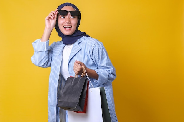 menina muçulmana abre os olhos de óculos de sol olhando para o lado segura muitas sacolas de compras