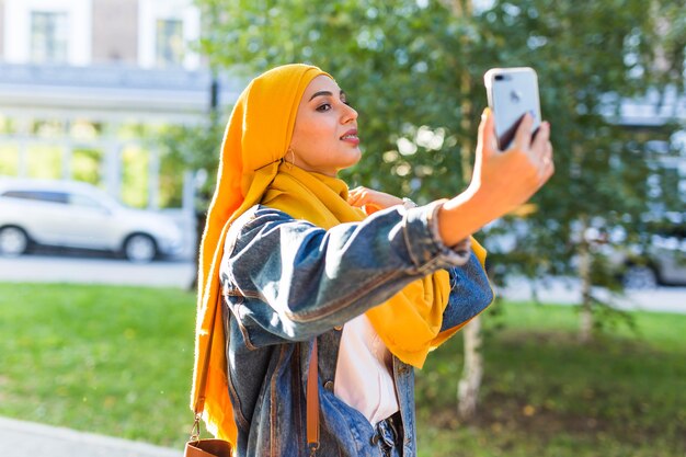 Menina muçulmana em hijab fazendo uma selfie ao telefone parada na rua da cidade