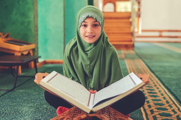 Menina muçulmana lendo um livro sagrado Alcorão dentro da mesquita