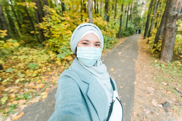 Menina muçulmana usando uma máscara médica fazendo uma selfie retrato de uma estudante árabe islâmica no parque