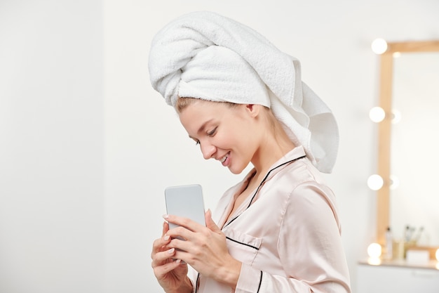 Menina muito sorridente com uma toalha na cabeça, segurando o smartphone na frente dela enquanto fotografa algo