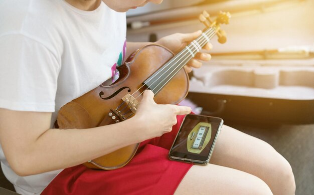 Menina mulher afina seu violino usando telefone elétrico