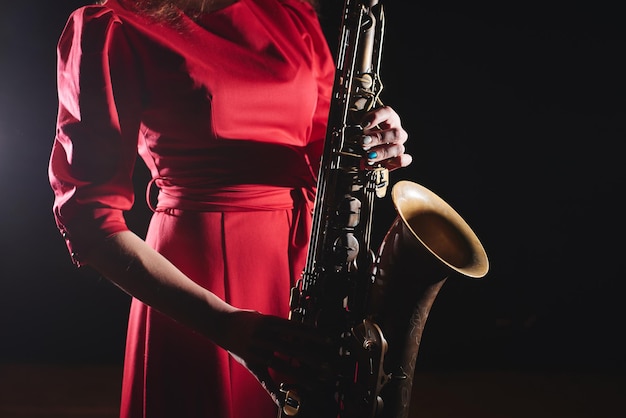 Menina músico em um vestido vermelho com um saxofone no palco