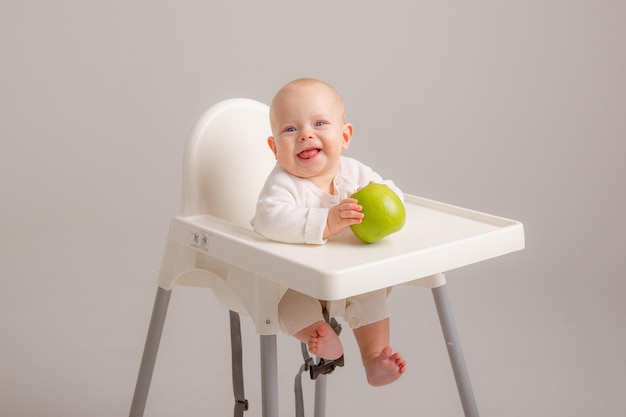 Menina na cadeira de bebê comendo maçãs no fundo branco Bebê primeiro alimento sólido