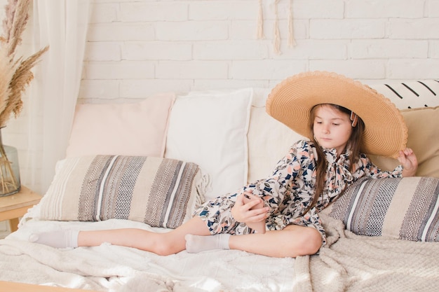 Foto menina na cama com um chapéu olha para o telefone