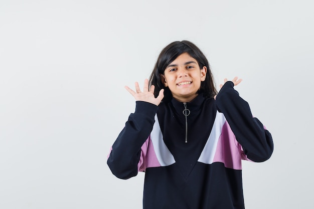 Menina na camisa, levantando as palmas das mãos vazias e olhando alegre, vista frontal.