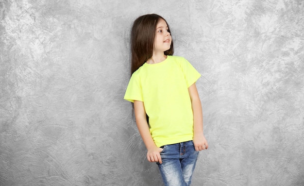 Menina na camiseta de cor em branco em pé contra a parede texturizada cinza