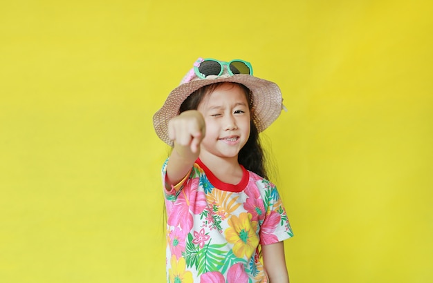 Foto menina na camiseta de verão, apontando para a câmera em fundo amarelo