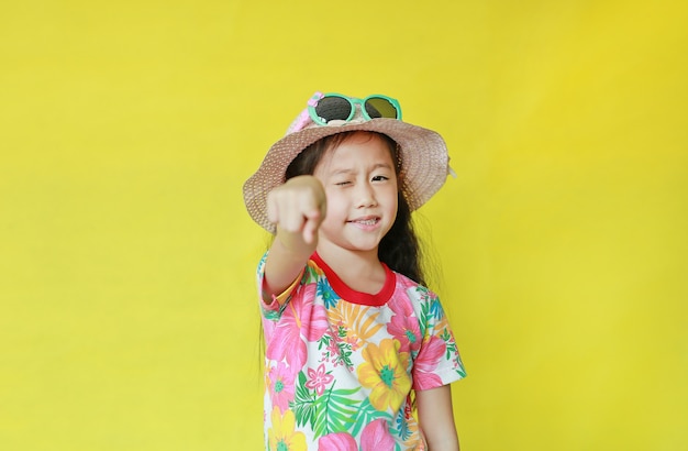 Menina na camiseta de verão, apontando para a câmera em fundo amarelo