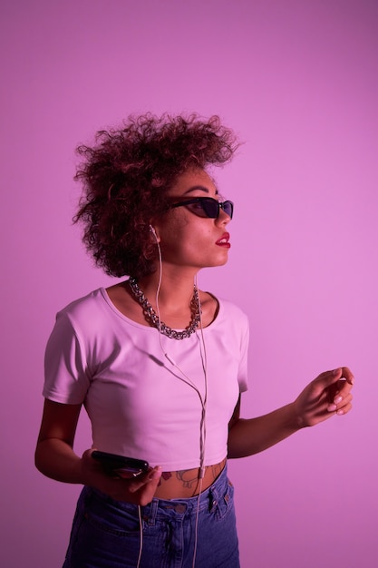 Foto menina na moda com cachos afro ouve e curte música com fones de ouvido na luz de néon rosa