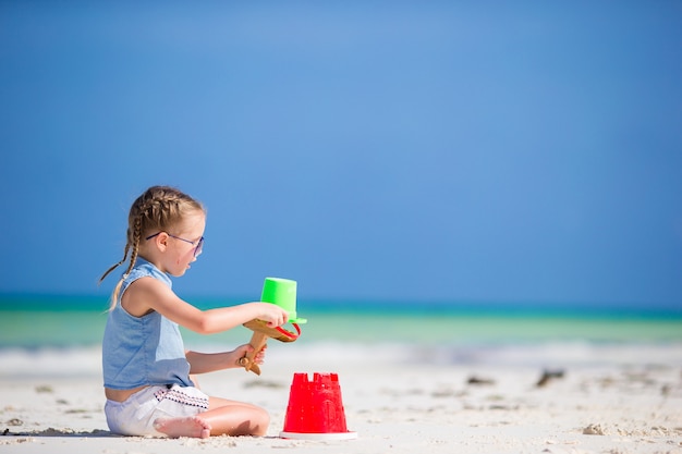 Menina na praia branca tropical fazendo castelo de areia