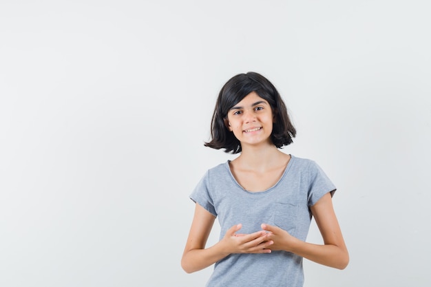 Menina na t-shirt em pé em pose de pensamento e olhando confiante, vista frontal.