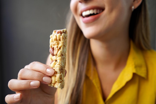 Menina não identificada comendo uma barra de cereais de nozes energética em fundo cinza