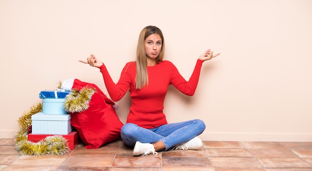 Menina nas férias de Natal, sentada no chão, apontando para as laterais, tendo dúvidas