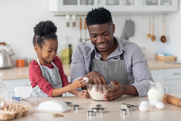 Menina negra adicionando ovos enquanto seu pai faz massa