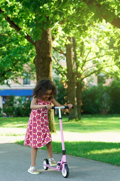 Menina negra com patinete em um parque da cidade