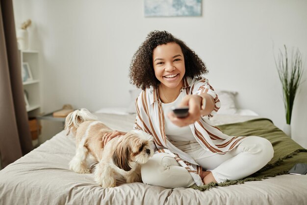 Foto menina negra feliz apontando o controle remoto para a câmera com cachorro de estimação