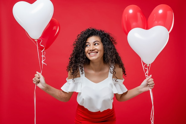 Menina negra muito alegre com balões de hélio coloridos isolados sobre o vermelho