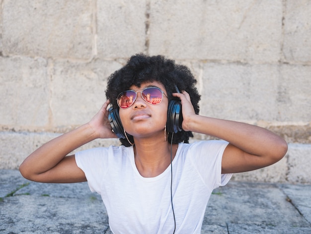 Menina negra ouvindo música com fones de ouvido, na rua, isolada