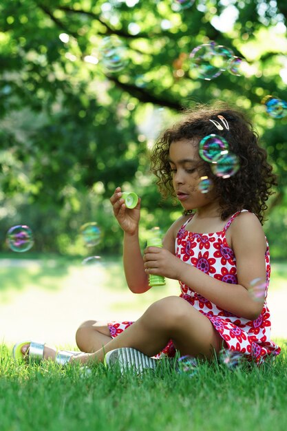 Menina negra soprando bolhas de sabão em um parque da cidade