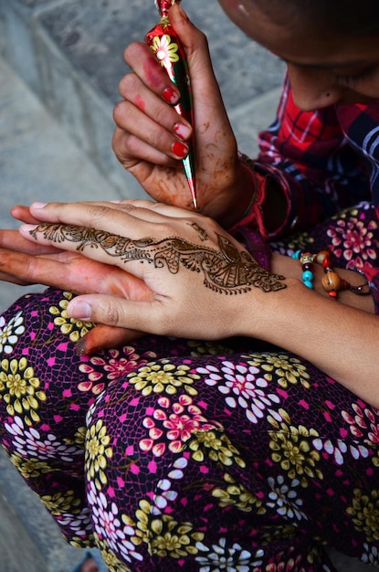 Menina nepalesa artista usa tinta henna escrever desenho pintura tatuagem de henna mehndi como padrão de arte corporal na mão de viajantes mulheres tailandesas entre visitas de viagem no mercado de bazar da cidade velha de thamel em Kathmandu Nepal