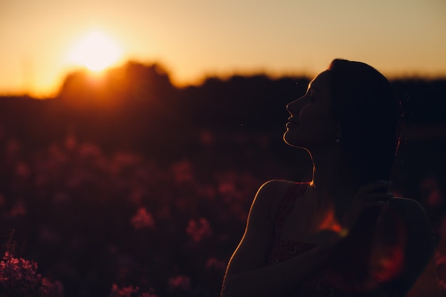 Menina no campo de flores desabrochando sally ao pôr do sol. flores lilás e mulher.