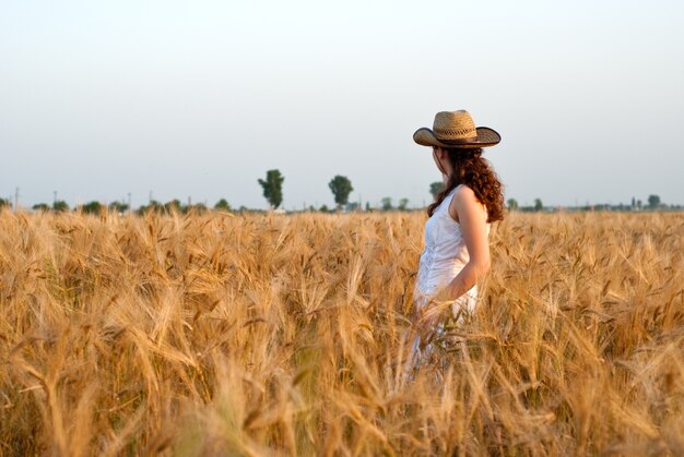 Menina no campo de trigo com vestido branco e chapéu stetson. Foco seletivo.