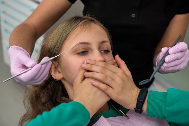 Menina no consultório do dentista fecha a boca com as mãos e não permite o exame inicial