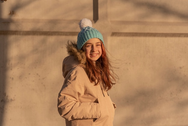 Menina no inverno com uma jaqueta bege. garota posando de azul com chapéu branco e roupas quentes de inverno.