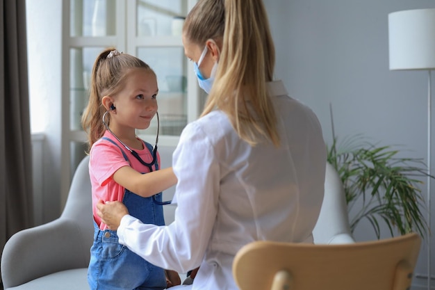 Menina no médico para um check-up. Criança ausculta os batimentos cardíacos do médico.