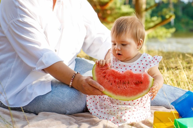 menina no parque no verão com a mãe experimenta melancia pela primeira vez