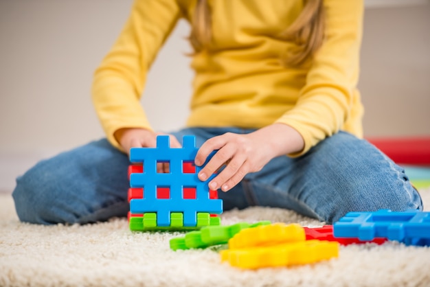 Menina no pulôver amarelo segurando fragmentos de lego.