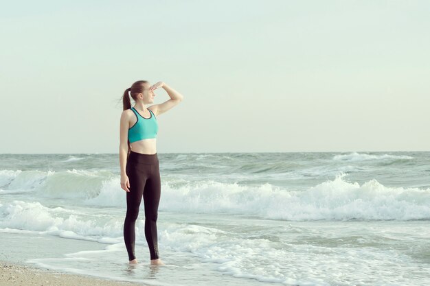 Menina no sportswear na praia, olhando para a distância.