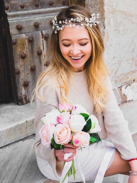 Menina nova do casamento do tártaro bonito na grinalda dos grânulos com um ramalhete das flores. Feche acima do retrato de uma noiva consideravelmente moderna atrativa que guarda o ramalhete das rosas. Foco seletivo