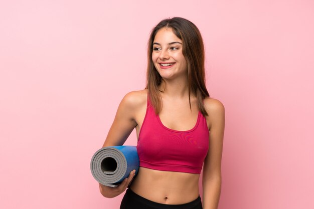 Menina nova do esporte sobre rosa isolada com uma esteira e um sorriso