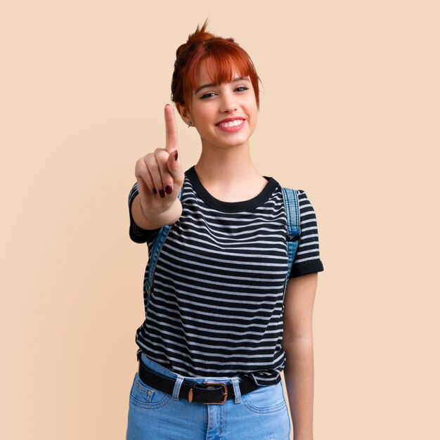 Foto menina nova do ruivo do estudante que conta o sinal do número um no fundo ocre. de volta à escola