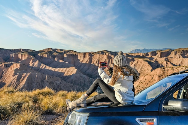 Menina observando a paisagem do deserto empoleirada no capô de um carro