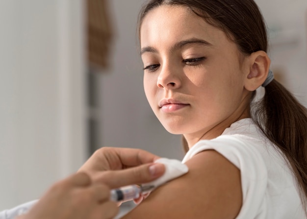 Foto menina observando enquanto o médico a está vacinando