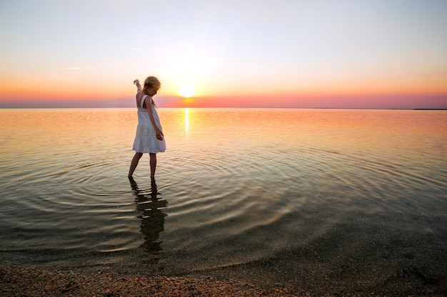 Menina olha o pôr do sol no mar